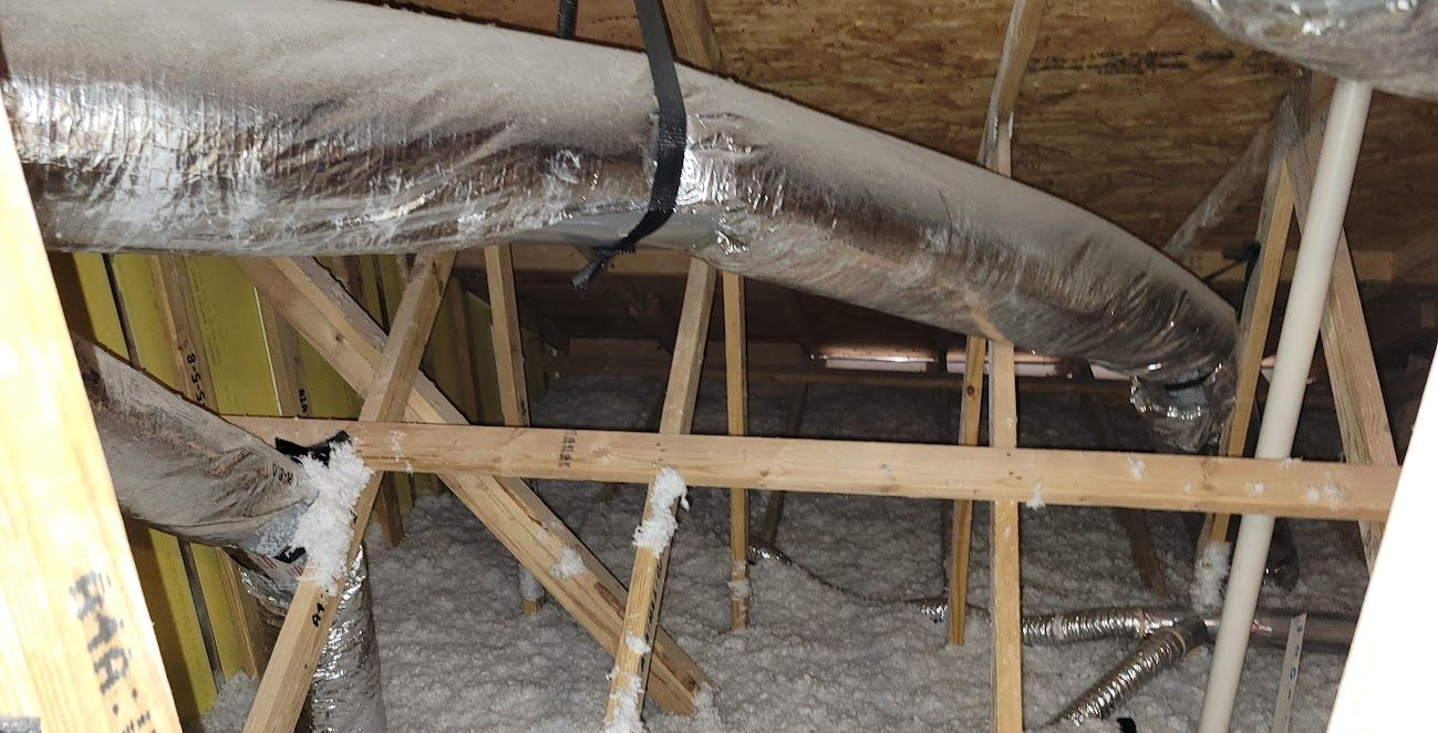 Exposed attic framing with insulated HVAC duct and white spray foam between wooden joists.