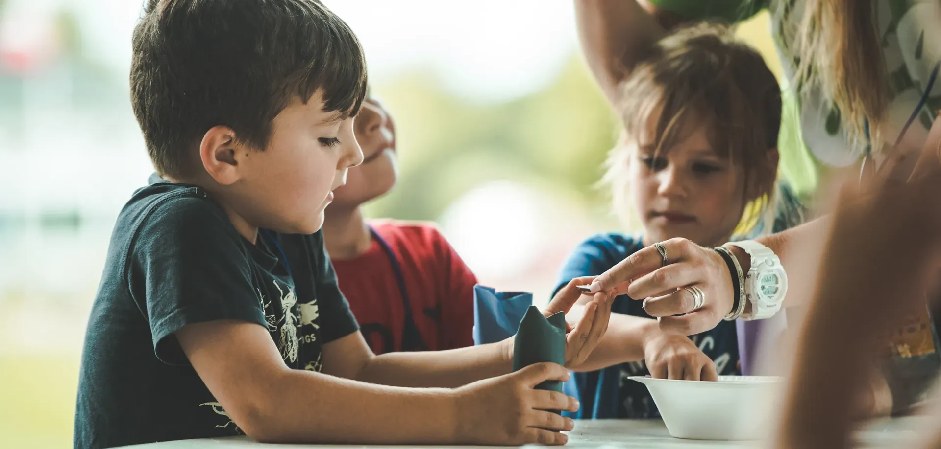 A group of children are sitting at a table playing with clay.