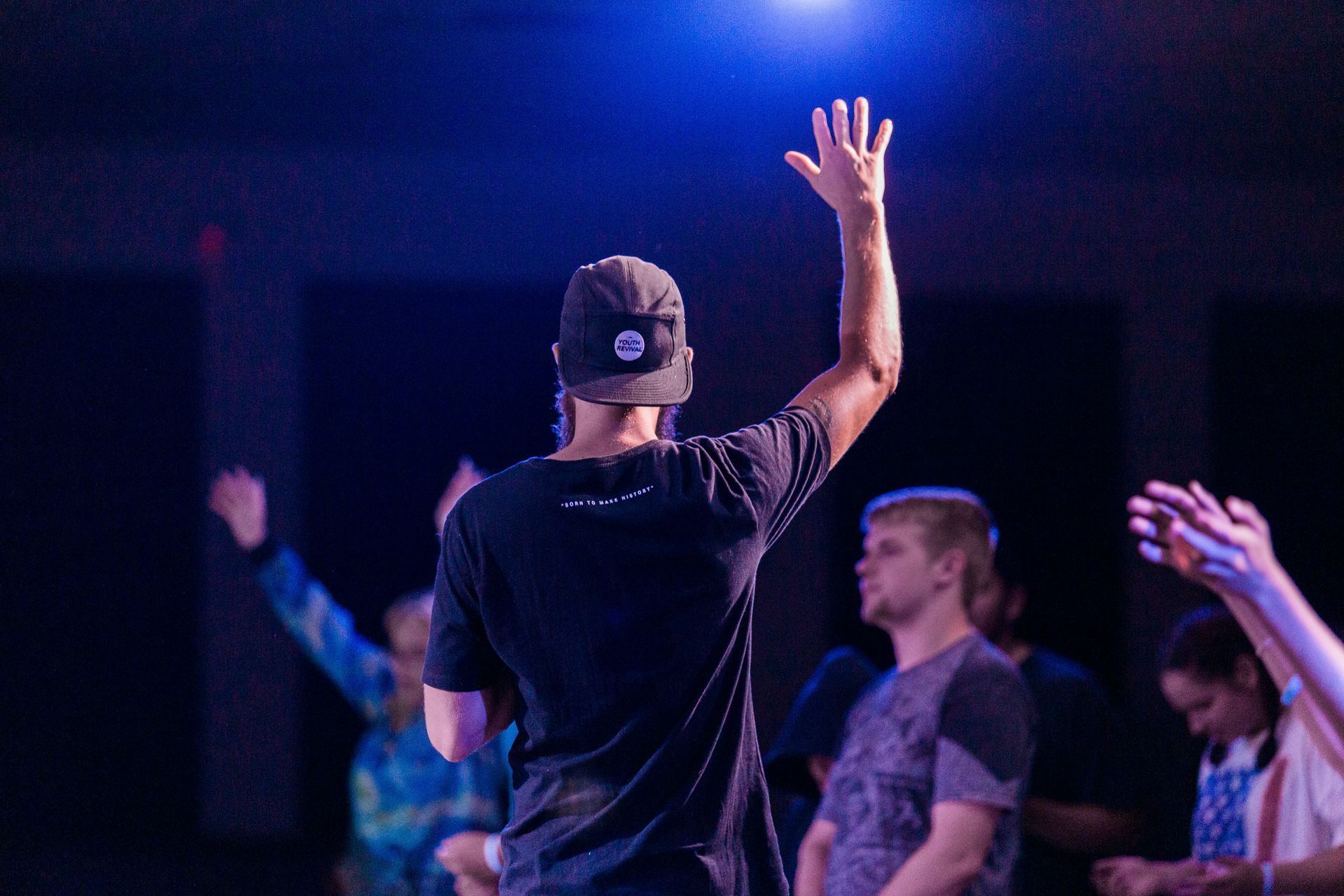 A man stands with hand raised in front of group of teens