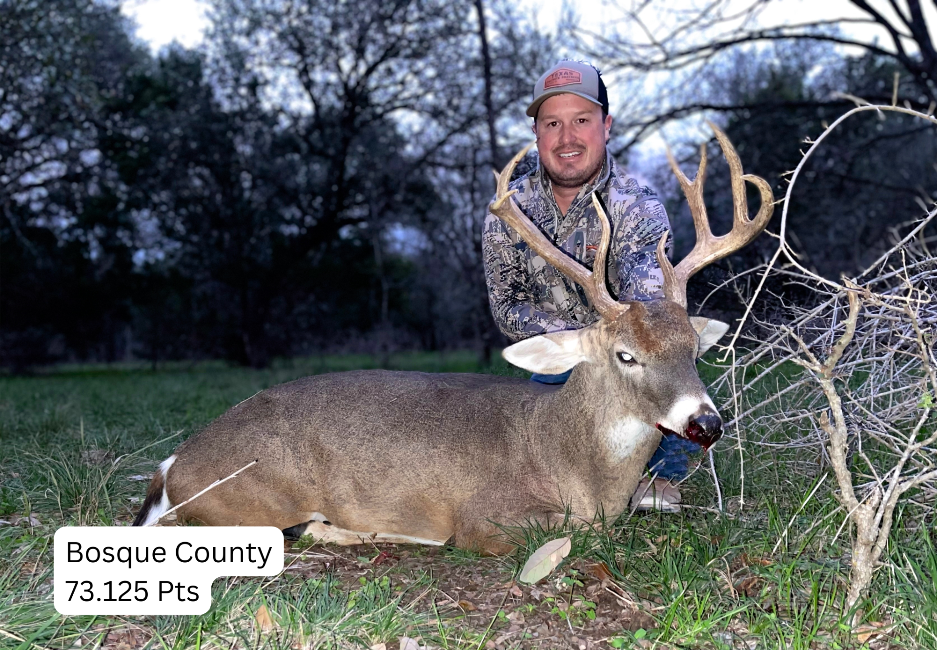 Man in camo smiles holding large buck in a grassy field in Bosque County.