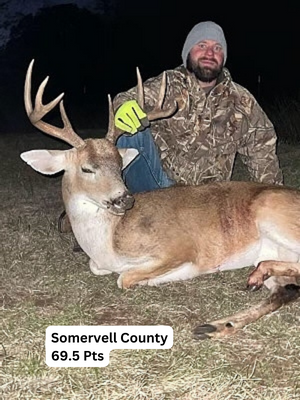 Man in camo kneeling next to a harvested deer with large antlers. Somervell County, 69.5 points.