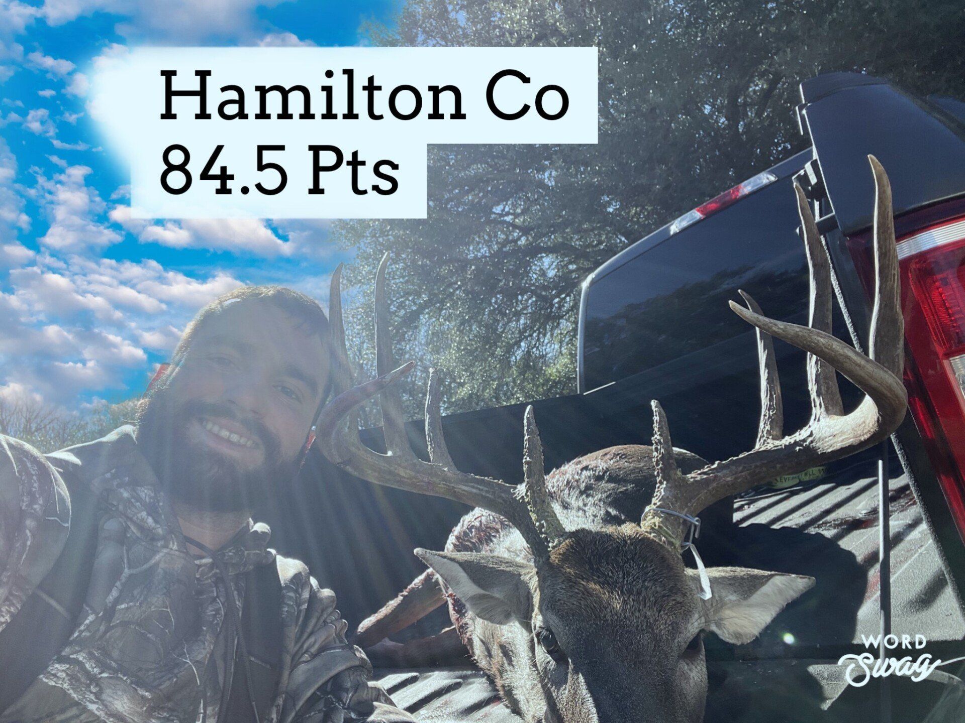 A man is standing next to a deer in the back of a truck.