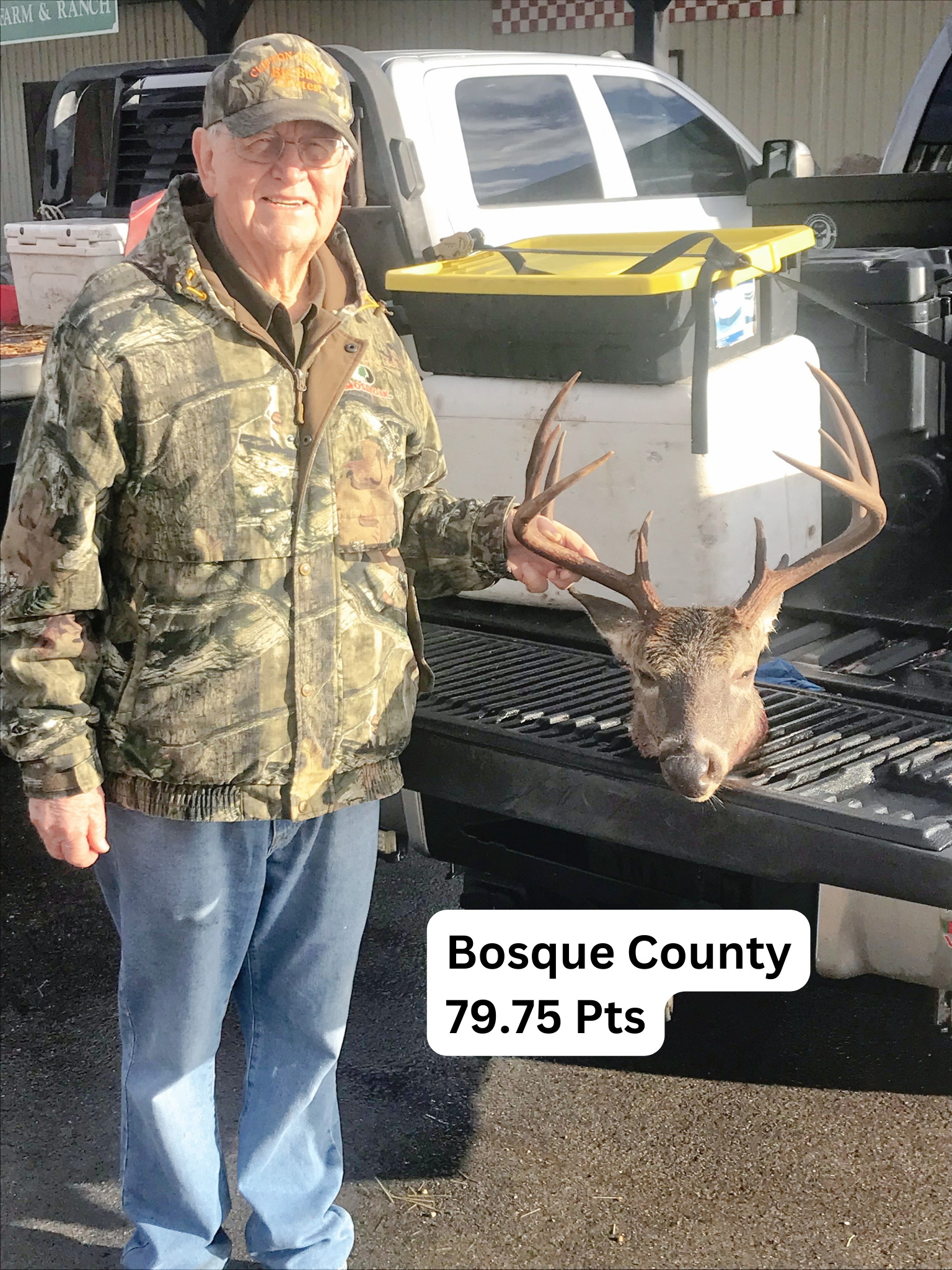A man is standing in front of a truck holding a deer head.