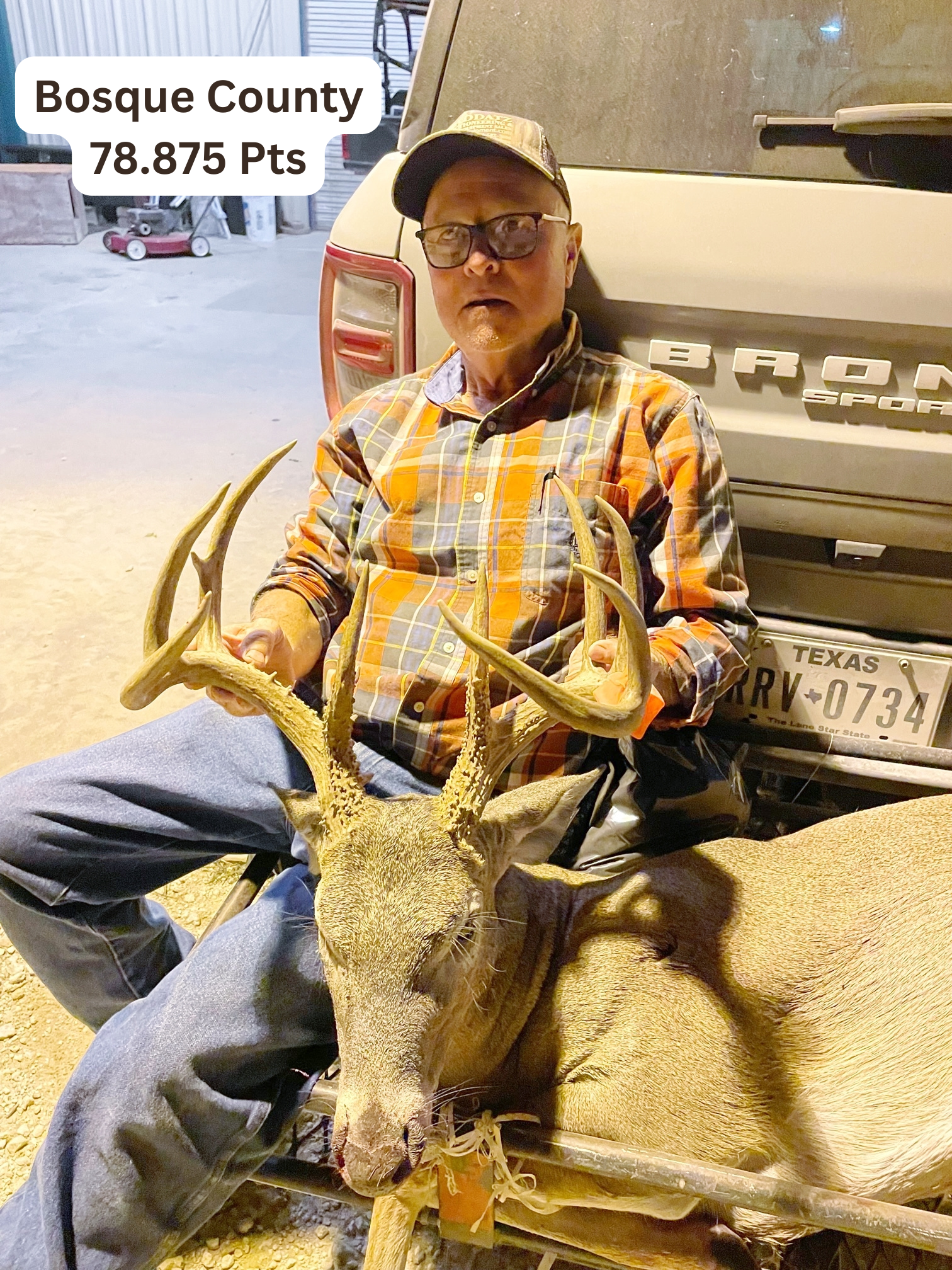 A man is sitting next to a car holding a deer.