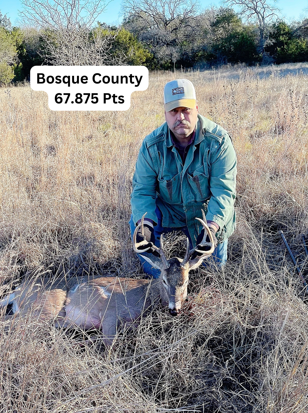 Man kneels beside a deer he hunted in Bosque County, Texas. He holds the antlers, and text reads 