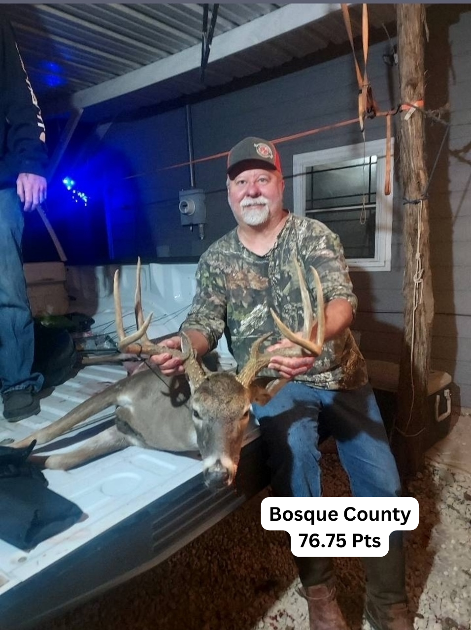 A man is sitting in the back of a truck holding a deer.