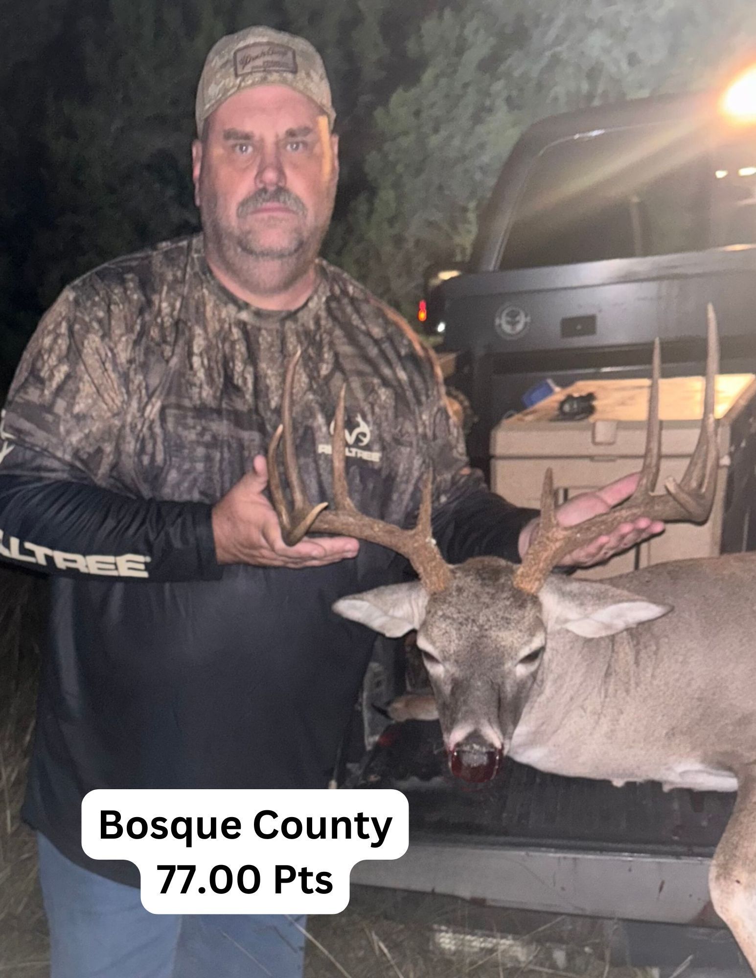 A man is holding a deer in front of a truck.