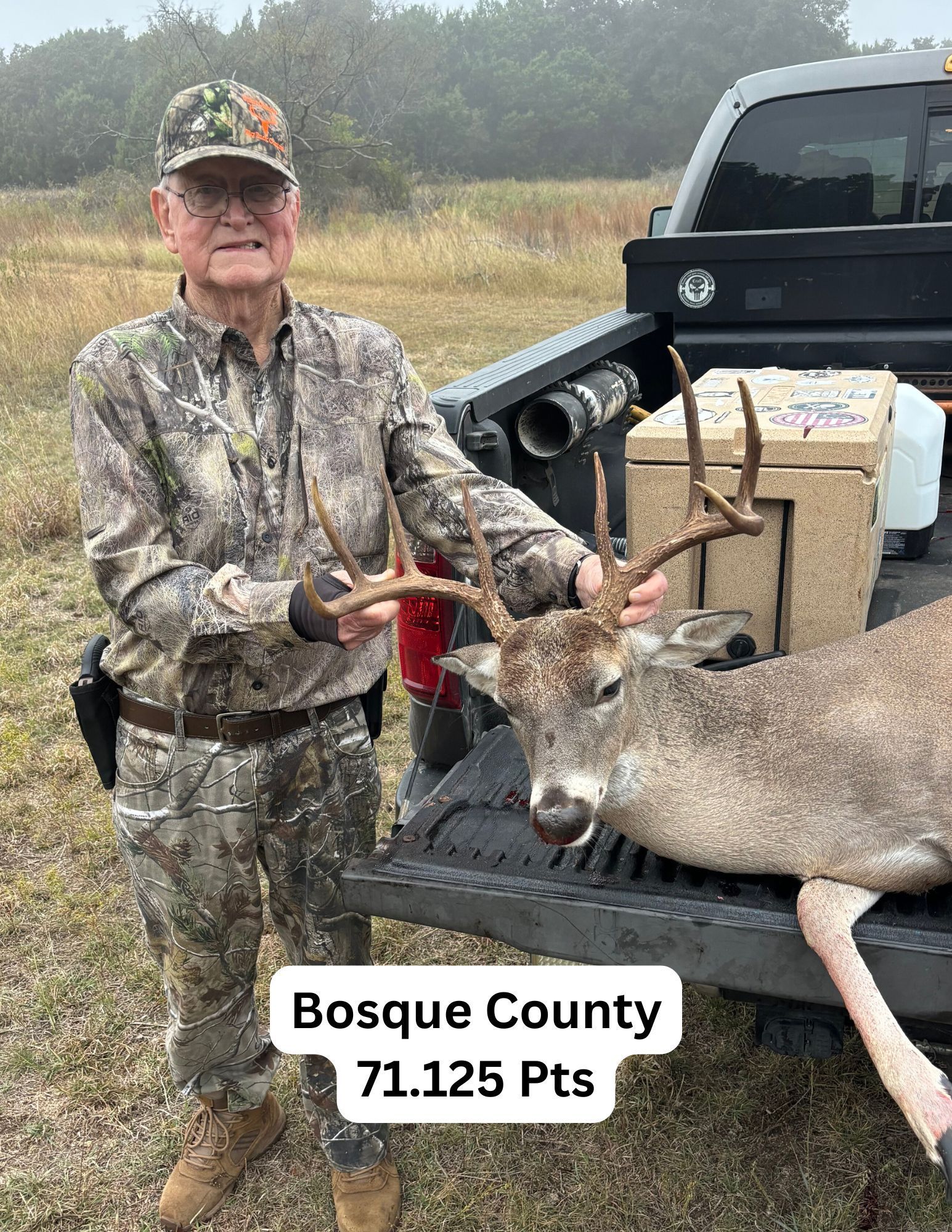 Man in camo with a buck he shot in Bosque County. He's smiling next to the deer on a truck bed.