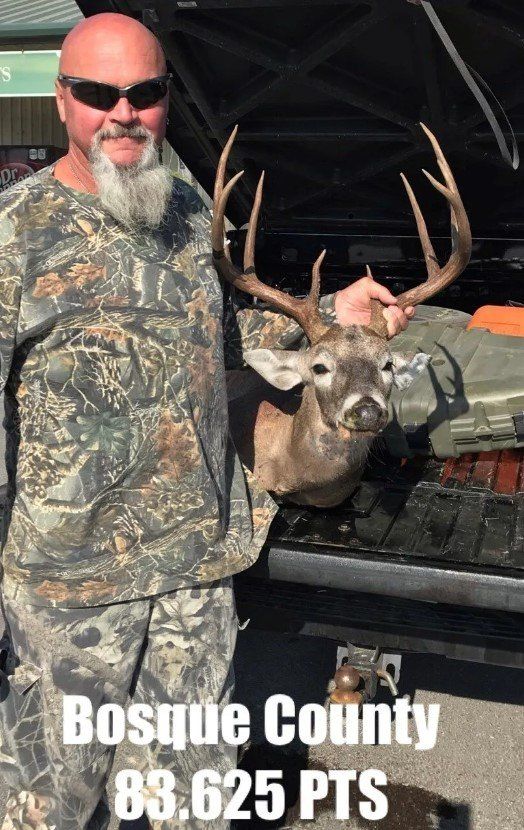 A man in a camo shirt is holding a deer in front of a truck.