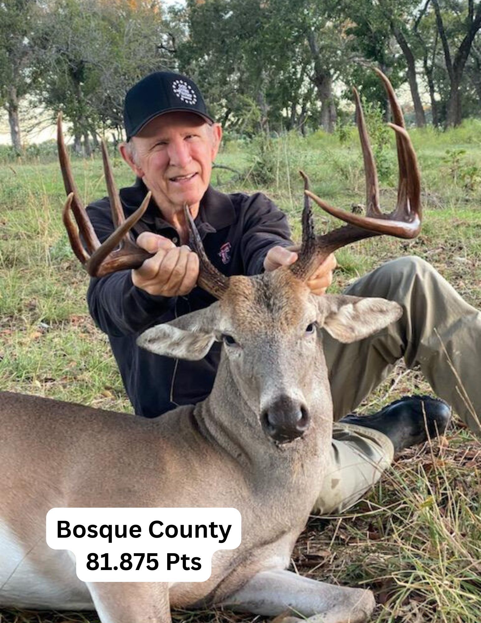 Man holding large deer antlers, Bosque County. He smiles, wearing a cap, with the deer at his lap.