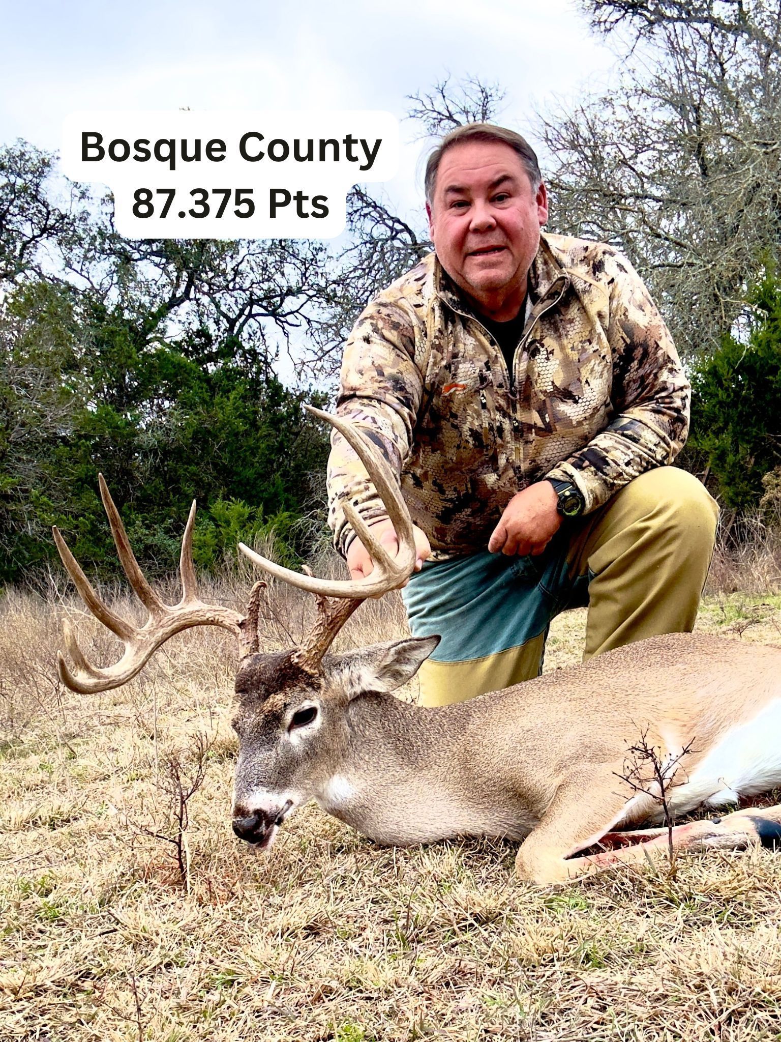 Man kneels beside a large deer he hunted in Bosque County. The deer has large antlers.