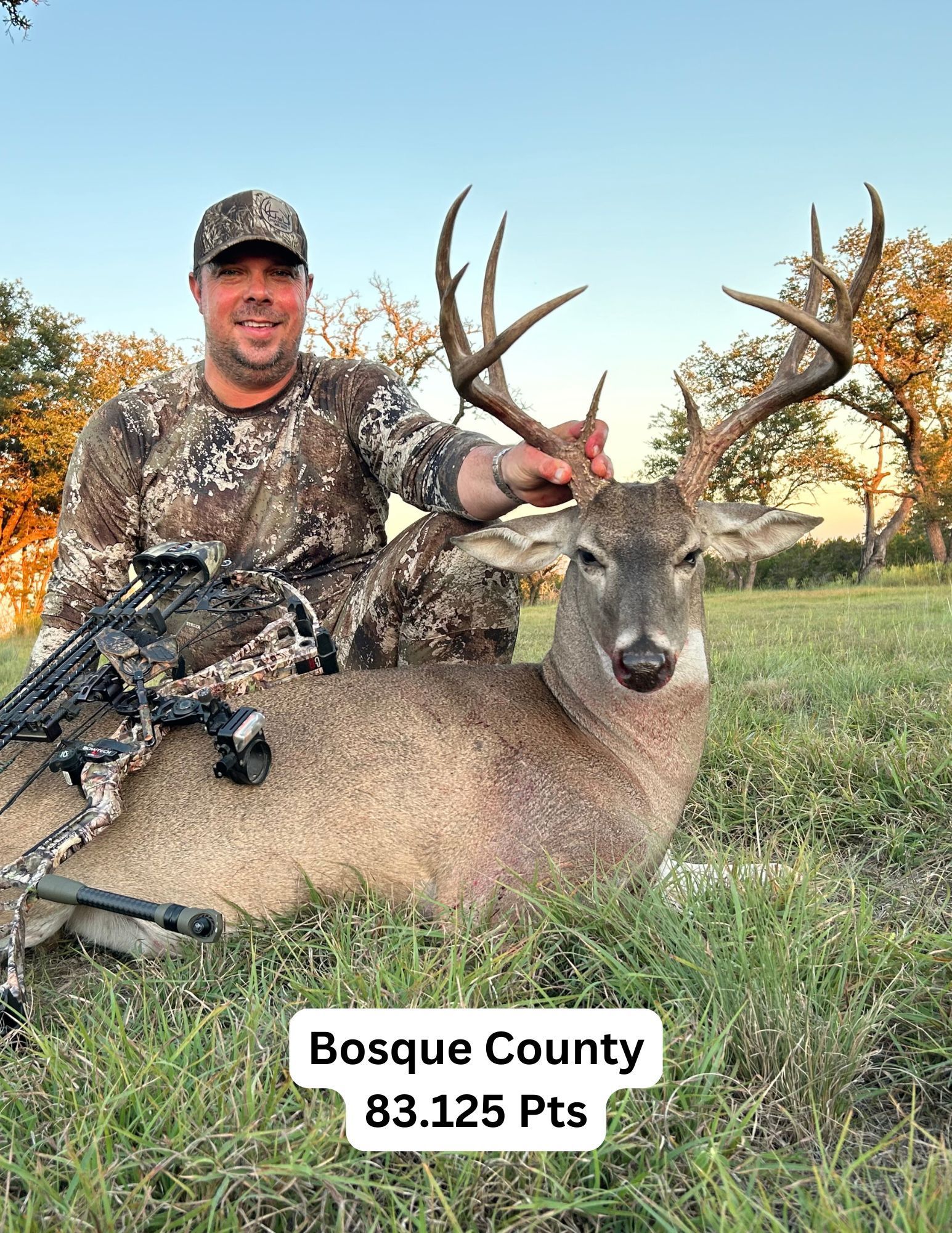 Man in camo with a large buck in Bosque County, Texas. He is smiling and touching the antlers.
