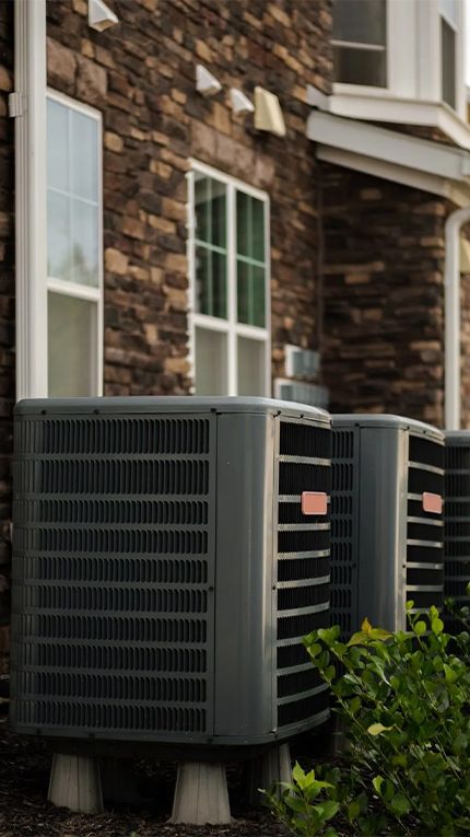 Two air conditioners are sitting on the side of a brick building.