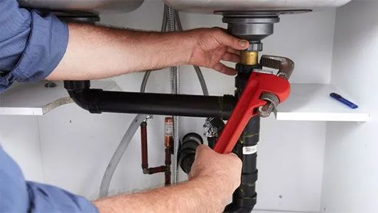 A man is fixing a sink with a wrench.