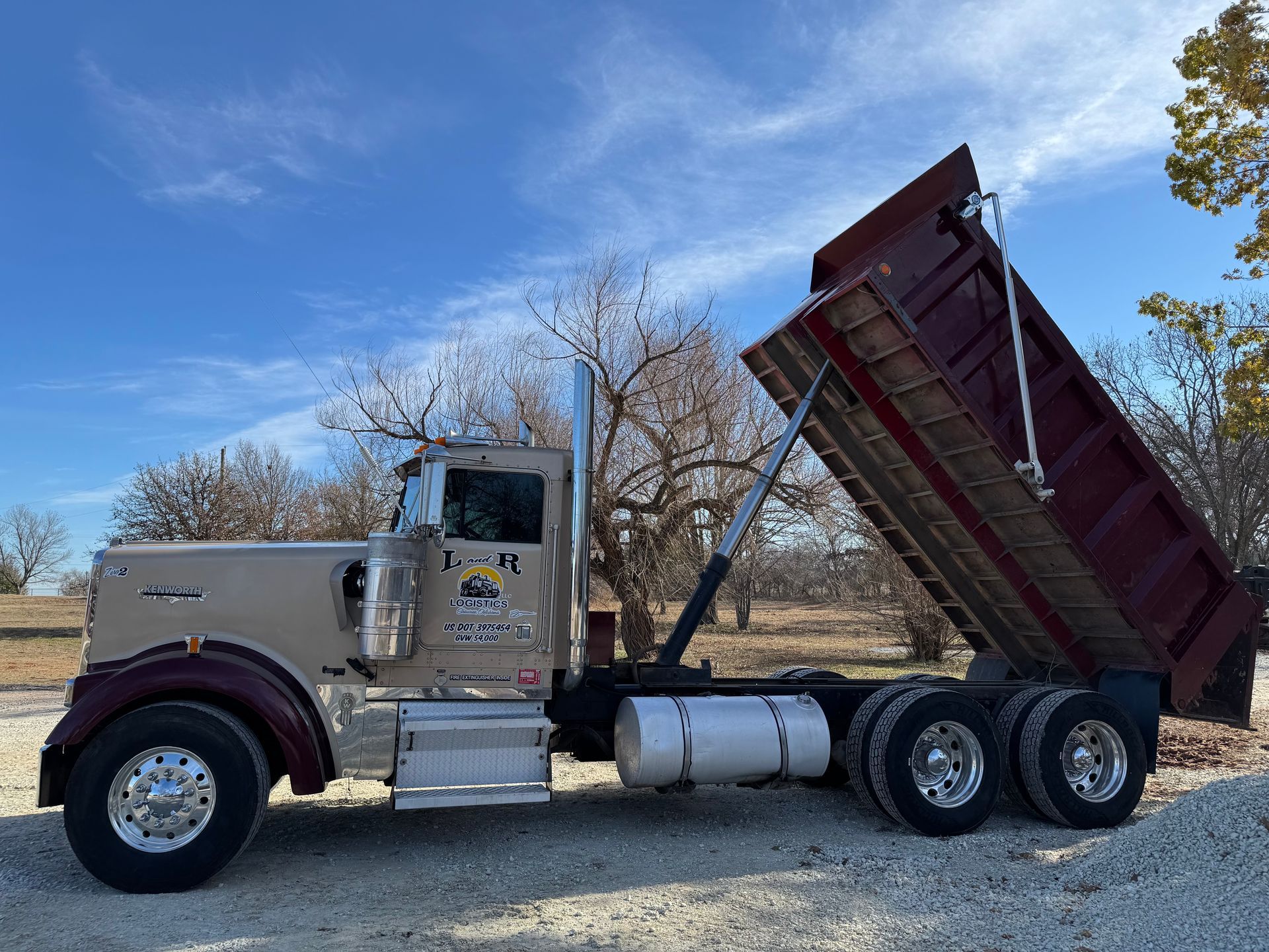 Silver dump truck with raised bed on a road under a blue sky