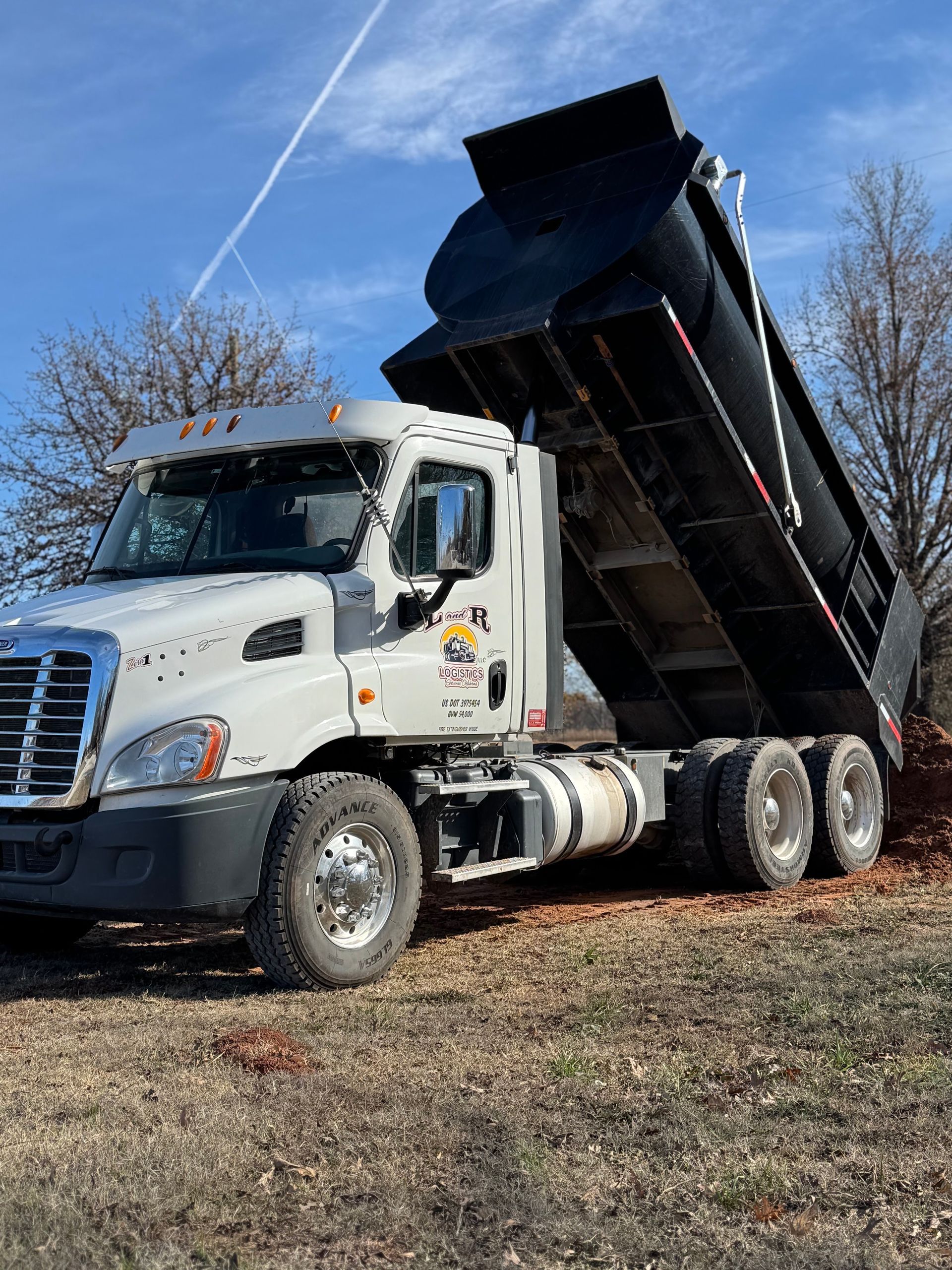 White dump truck with raised black bed parked on a grassy field under a blue sky