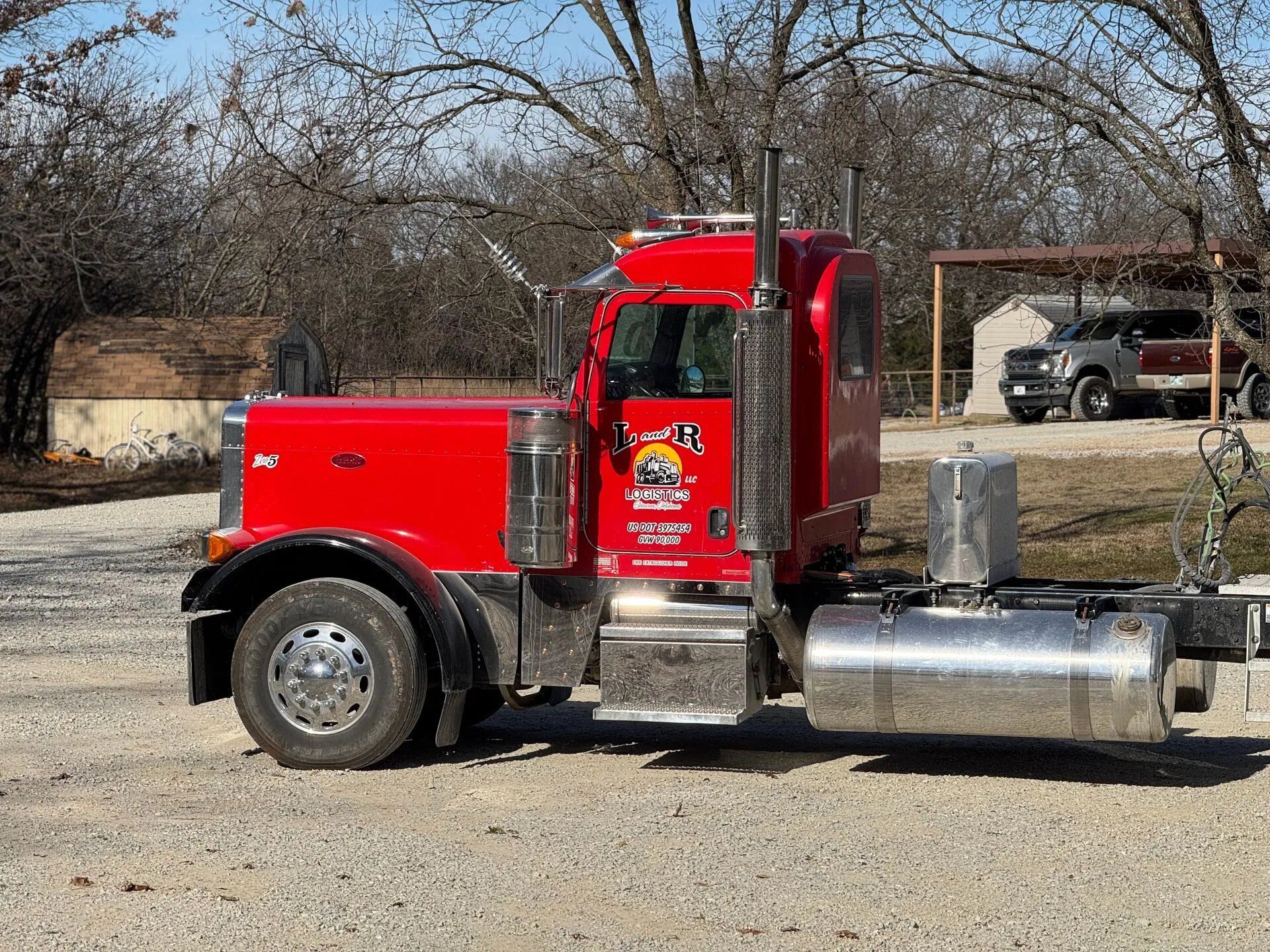 Red semi truck parked outdoors beside a fence and bare trees