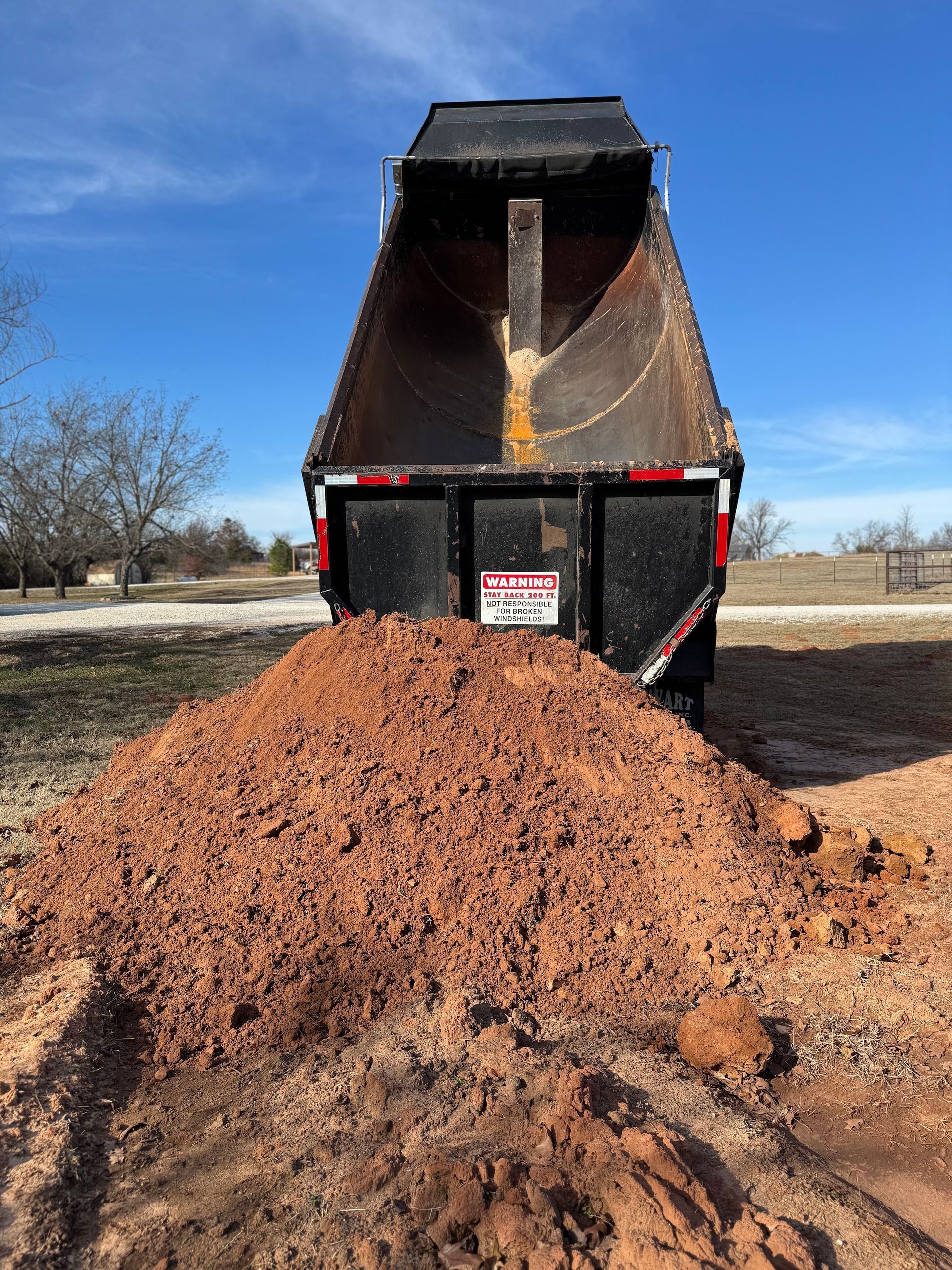 Black dump trailer unloading a large pile of wood chips outdoors on a sunny day