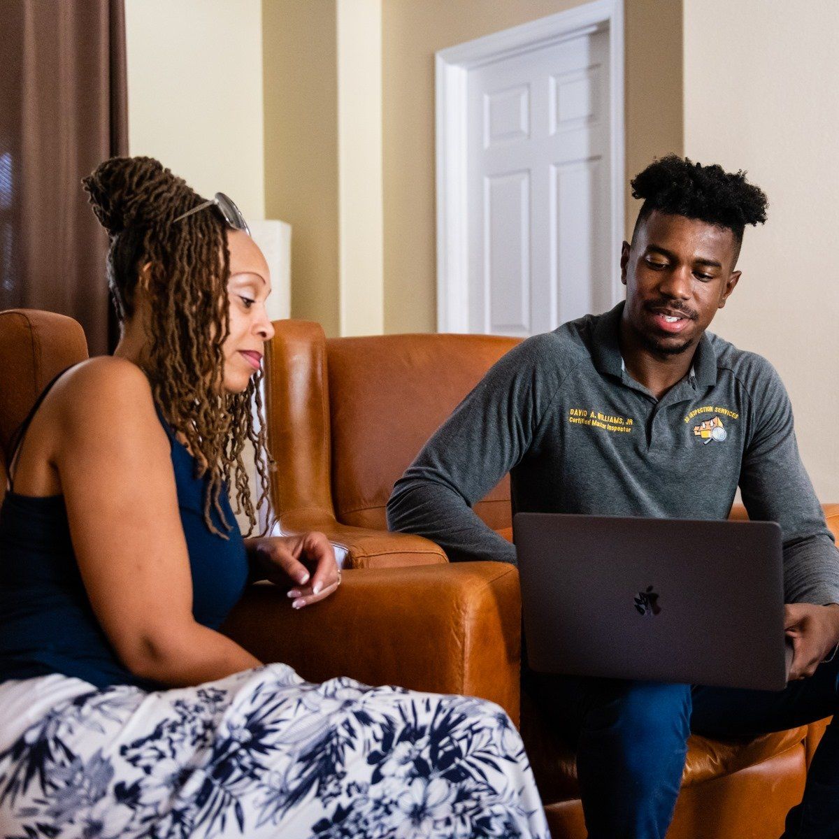 Two people sitting on a leather sofa, one reviewing information on a laptop while the other looks on.