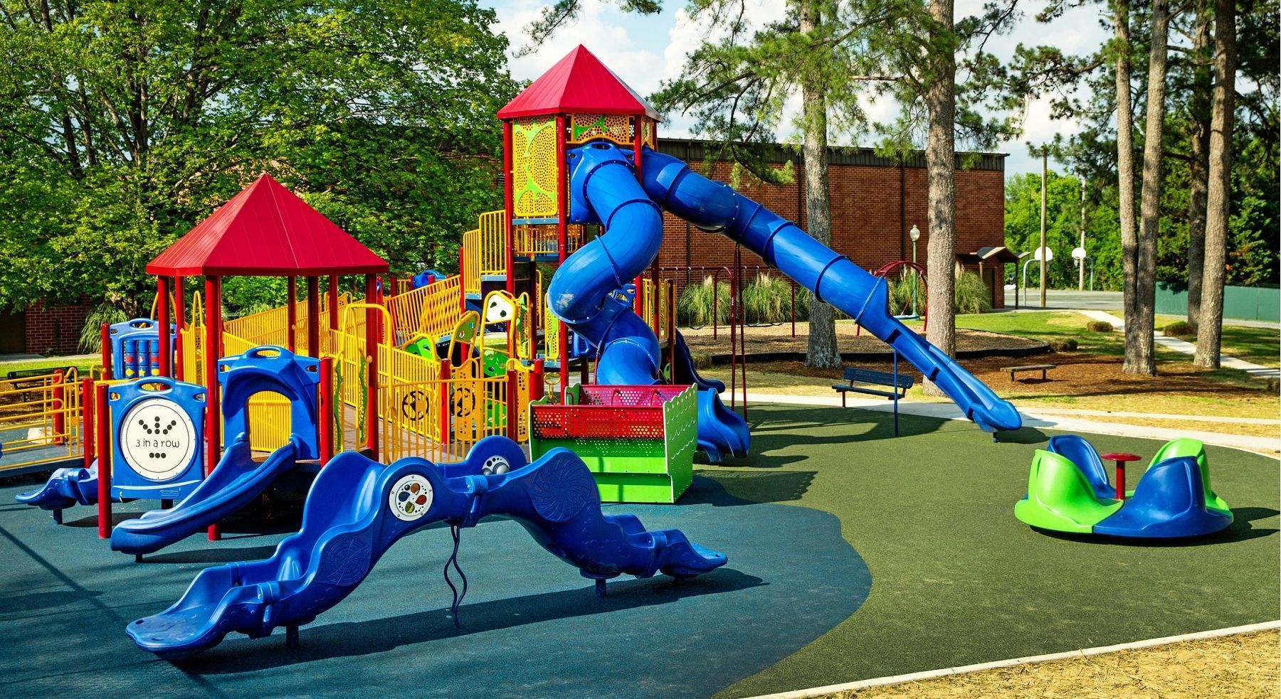 Colorful playground equipment with blue slides, a climbing tower, and a green-and-blue teeter-totter on a rubber surface.