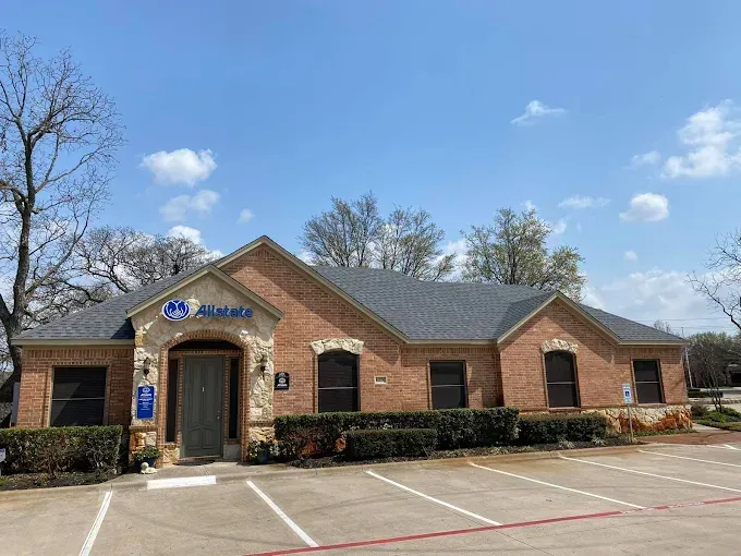 Allstate insurance office building with brick facade, blue sign, and small trees in a parking lot.
