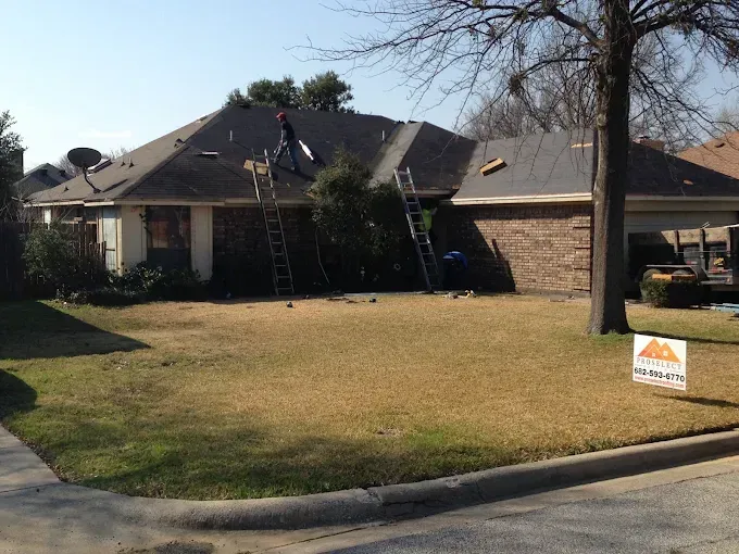 Roofers on a house with ladders; removing shingles under a sunny sky.