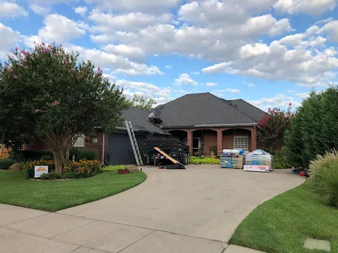 House with new dark roof, driveway, and landscaping; roofing materials in the yard.