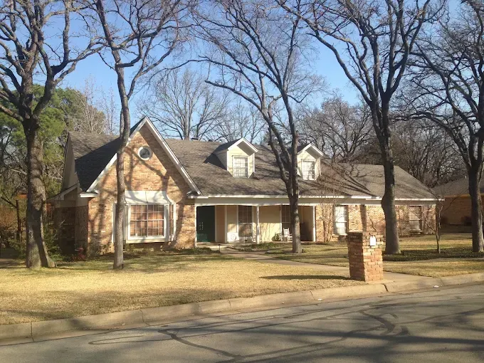 Brick house with dormers under leafless trees on a sunny day.
