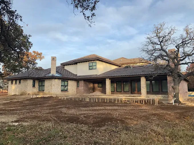 Large house with brown roof, stone and beige walls, windows, and chimney; in a field.