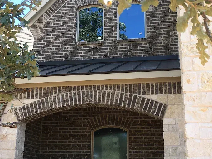 Brick building facade with arched entry and windows; blue sky reflected in one.