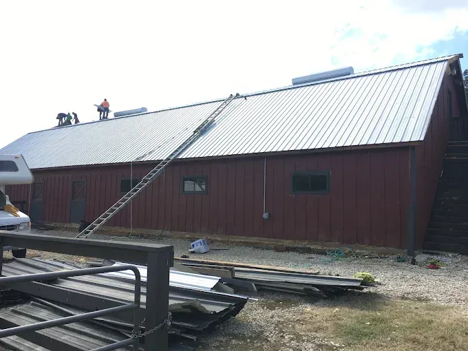 Red barn with a metal roof; workers on the roof. Ladder leading up.