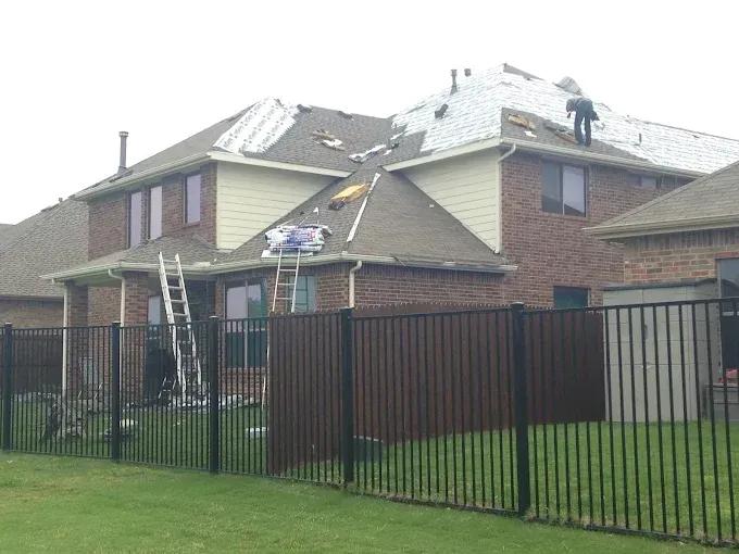 Roofers working on a residential home, removing old shingles and installing new ones; ladders, overcast day.