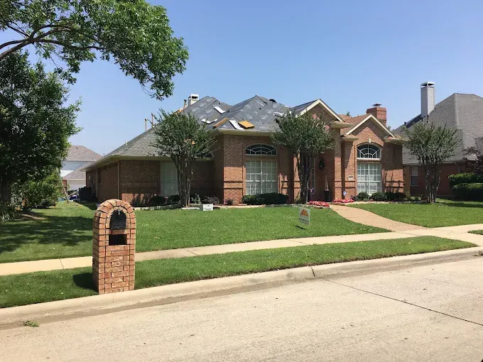Brick house with damaged roof and green lawn on a sunny day.