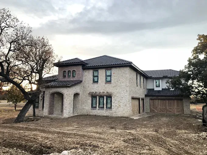 Two-story house with stone facade, arched entry, dark roof, cloudy sky.
