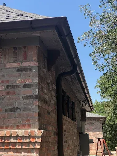 Brown brick building with dark gutters and a downspout against a blue sky.