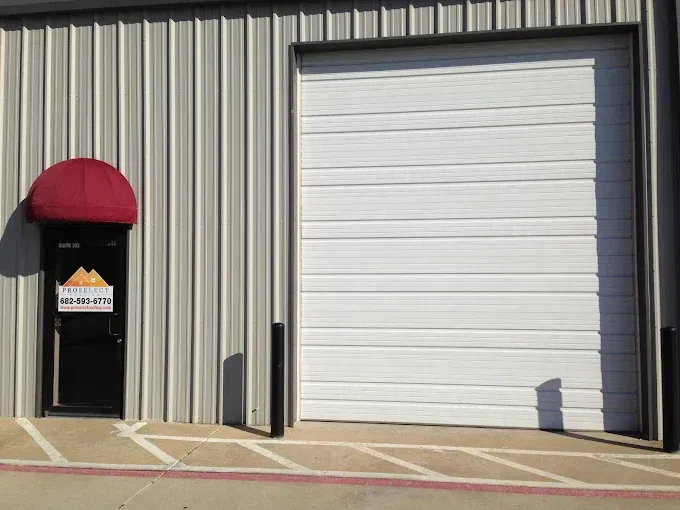 White garage door beside a black door with a red awning. Building has vertical metal siding.