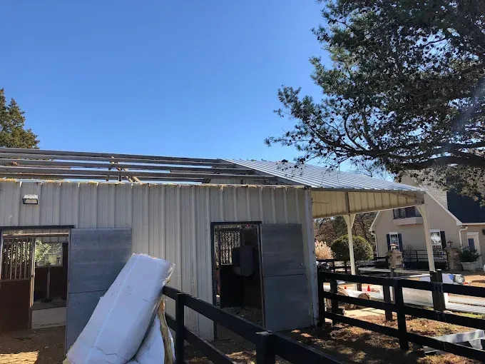 Barn with missing roof, sunny day. White metal siding, dark fence in foreground.