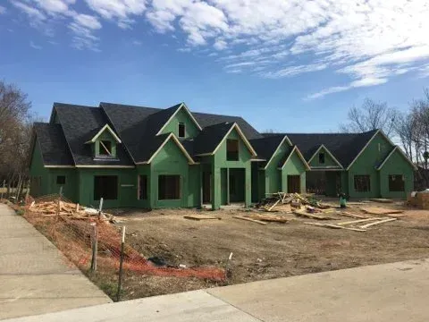 A house under construction with a dark roof and green siding on a sunny day.