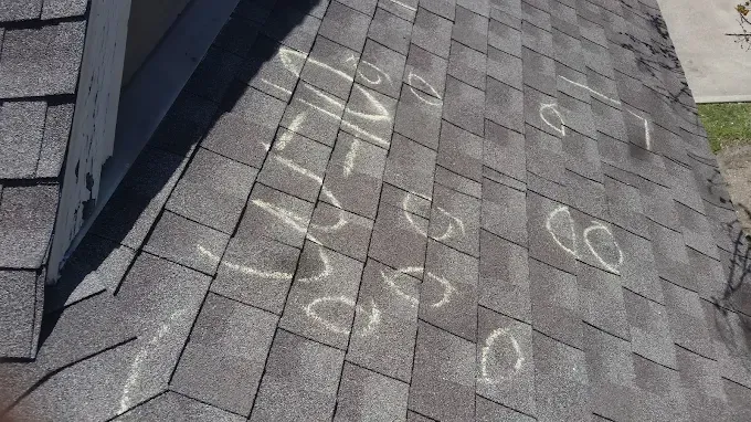 Asphalt shingle roof with several chalk circles marking hail damage.