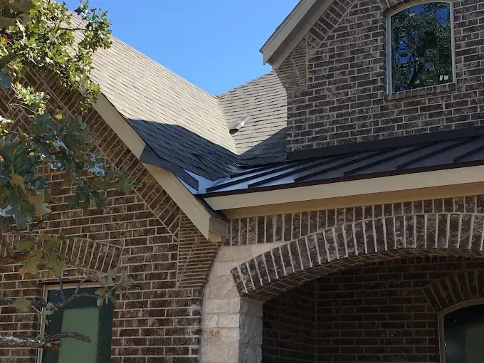 Brick home exterior with dark metal roof, arched porch, and blue sky.