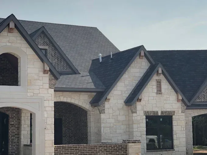 Two-story house with stone facade, dark roof, arched doorway, and brick accents.
