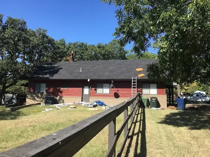 House with dark roof, red siding, and green lawn. Construction materials and ladder visible.