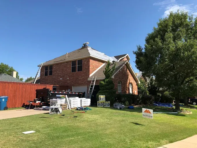 House with new roof under construction; materials and ladders on the lawn.