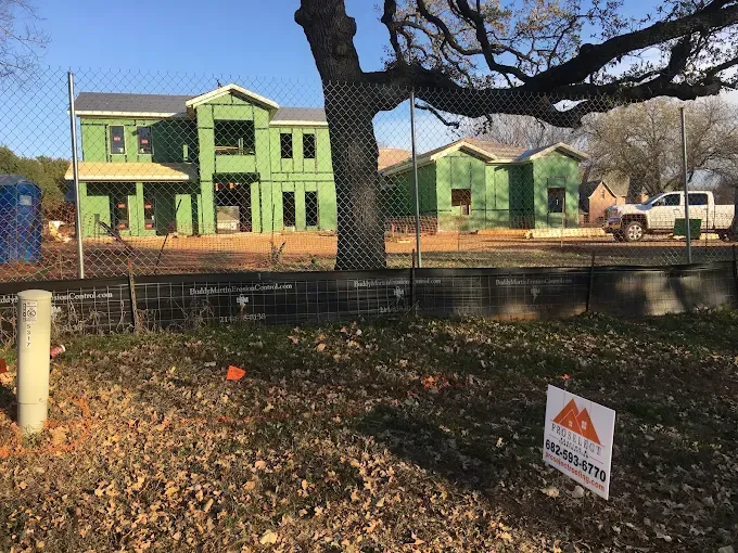New houses under construction behind a chain link fence. Green siding and a white truck are visible.