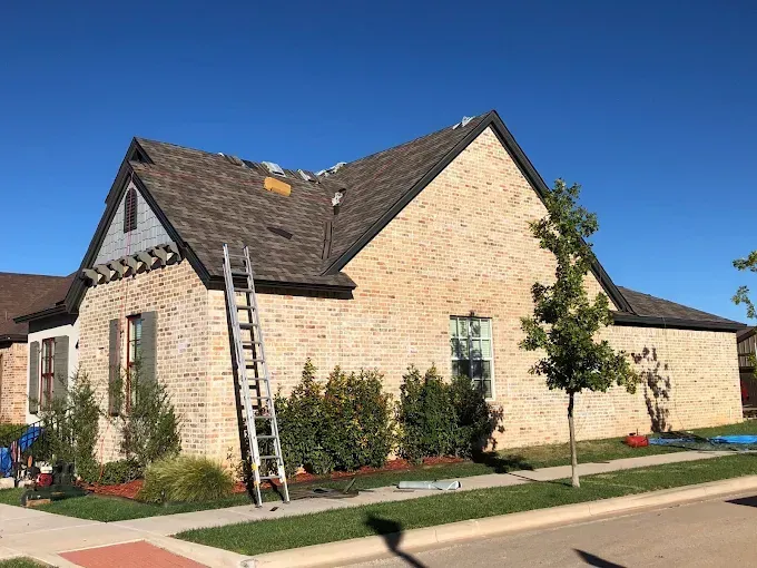 House with partially replaced brown roof; ladder leaned against the side. Sunny day.