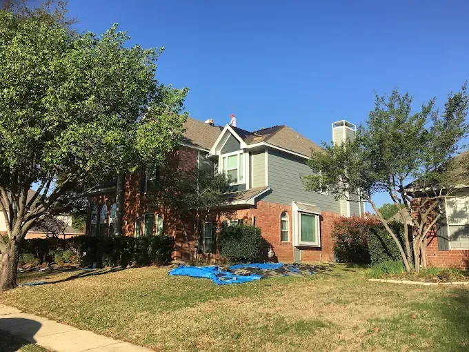 Two-story house with brick and blue siding, surrounded by trees and a lawn.