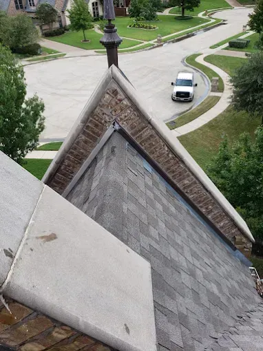 View from a rooftop: asphalt shingles, brick trim, a chimney, and a street with a white van.
