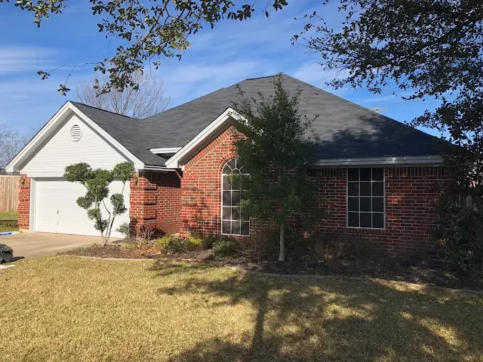 Brick house with dark roof and white garage door under a bright blue sky.