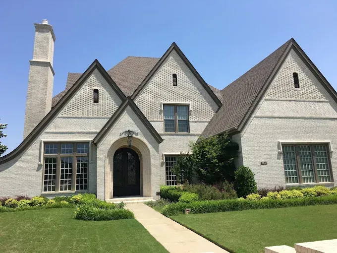 A two-story white brick house with a dark brown roof and a green lawn under a blue sky.