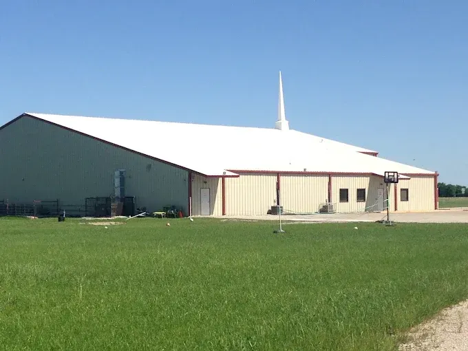 Light tan church building with white roof, steeple, and green lawn.